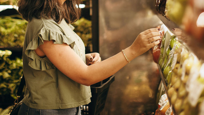 Frau wählt Apfel aus Obstregal im Supermarkt